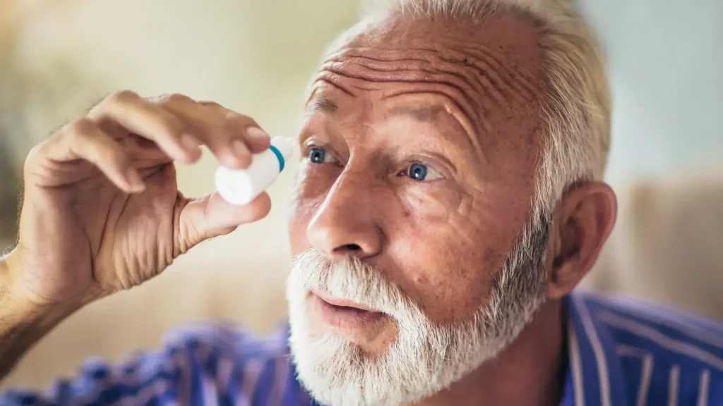 An older individual applying eye drops on their eye.