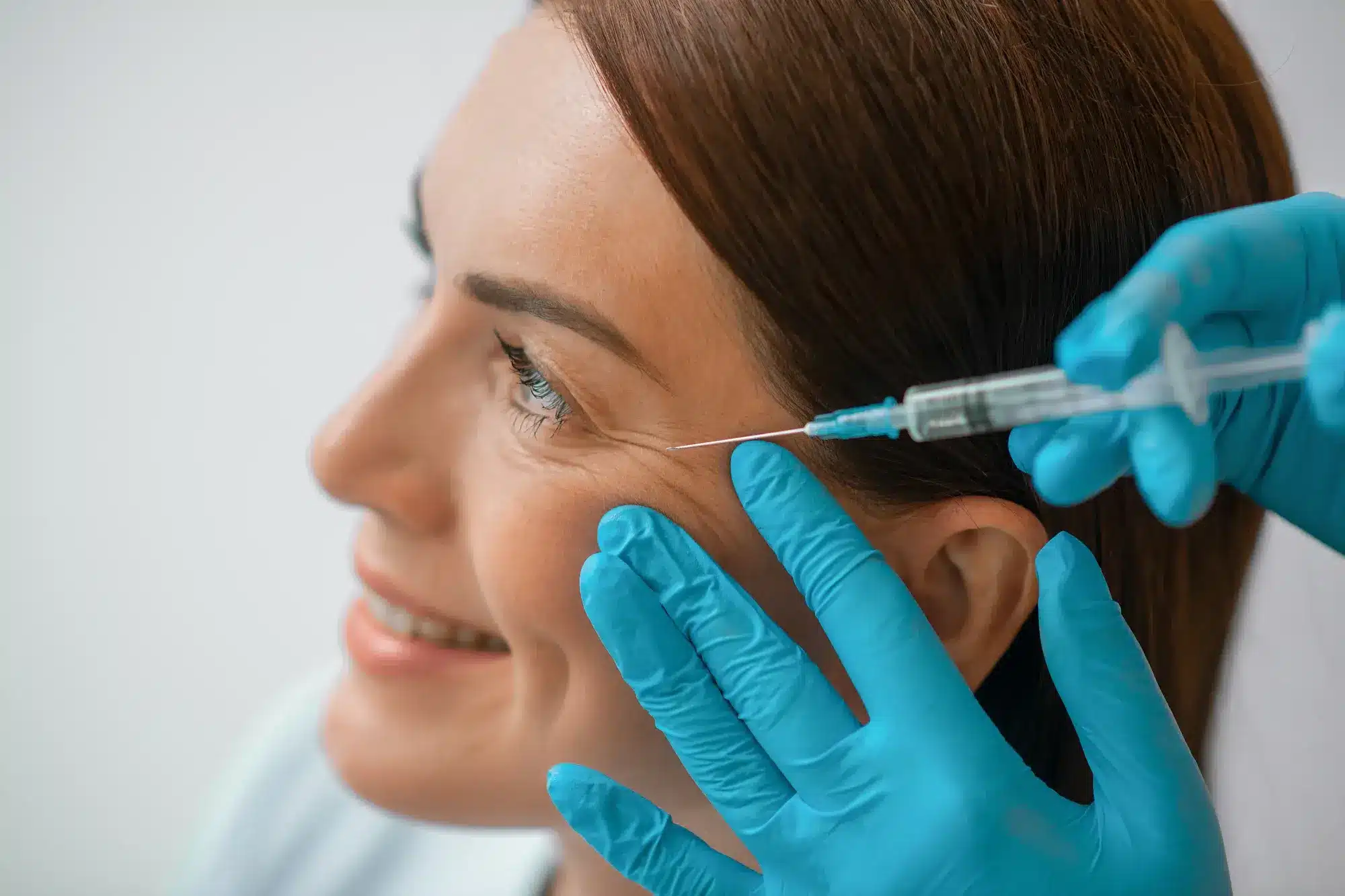 A smiling female patient receiving Botox injections for eye wrinkles