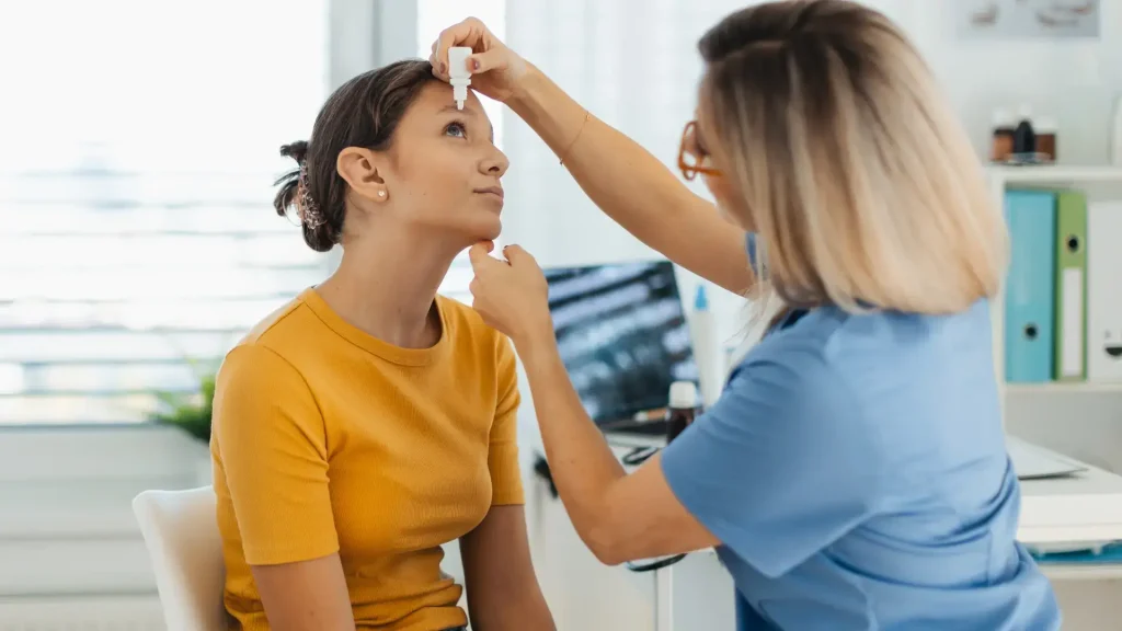 A medical professional administering eye drop treatment on a patient.