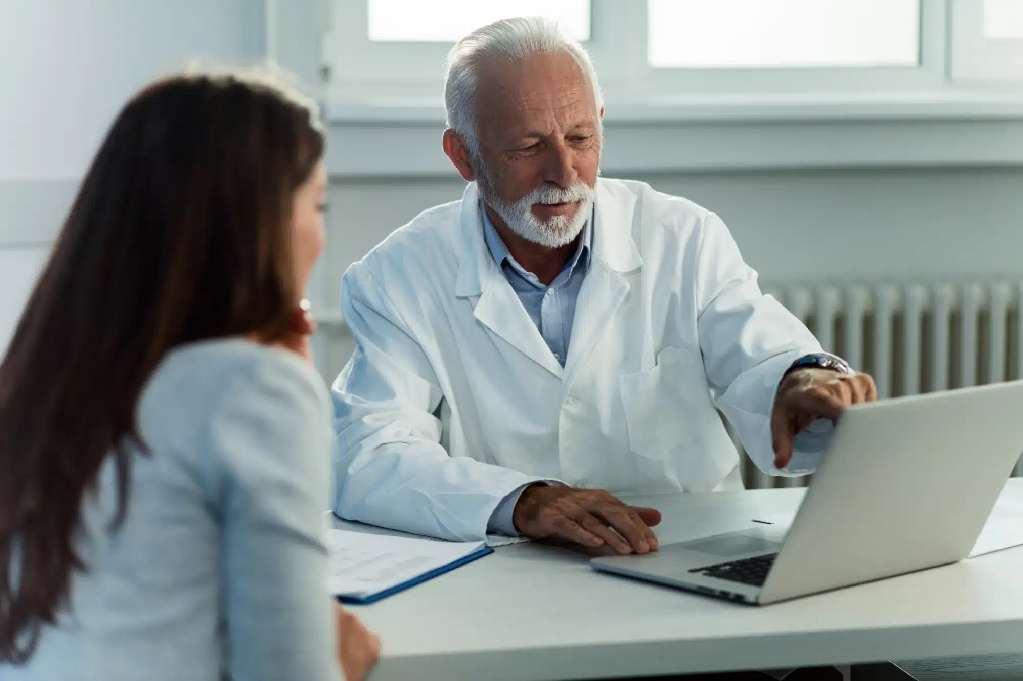 Older doctor showing to a younger colleague something on the screen of his laptop