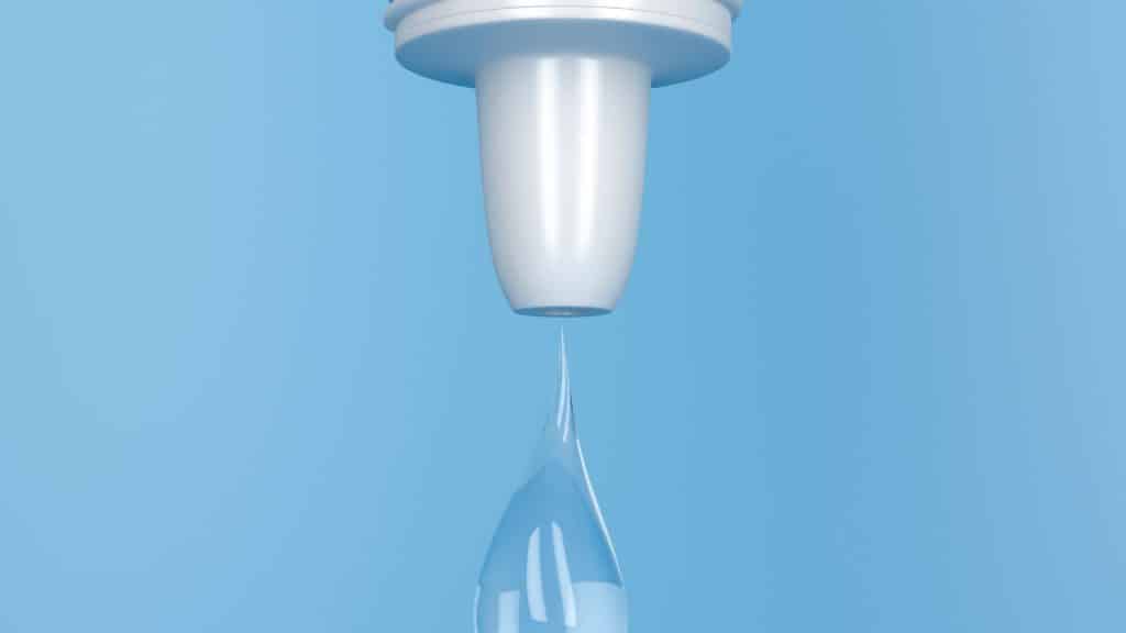 Close-up of a white water filter against a light blue background, with a single droplet of clear water falling from the filter.