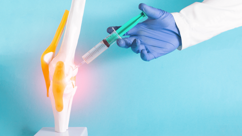 A medical professional wearing a blue glove injects a syringe into a knee joint model against a light blue background. The knee joint model shows highlighted areas in yellow and orange.