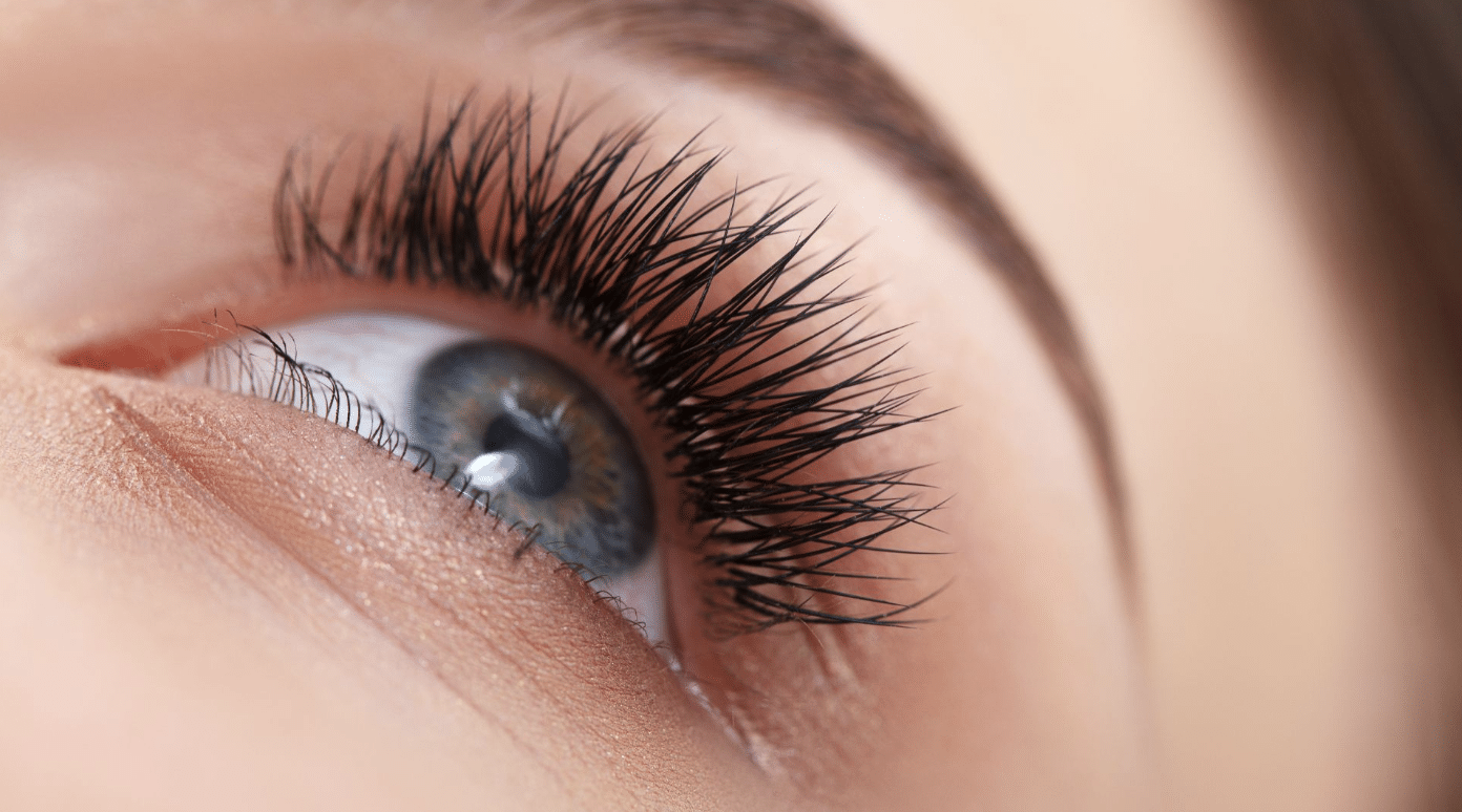 Close-up of a person's eye looking upward. The focus is on the long eyelashes and the detailed iris, which has flecks of different colors. The skin around the eye is smooth and the eyebrow is partially visible. The lighting highlights the texture of the eyelashes.