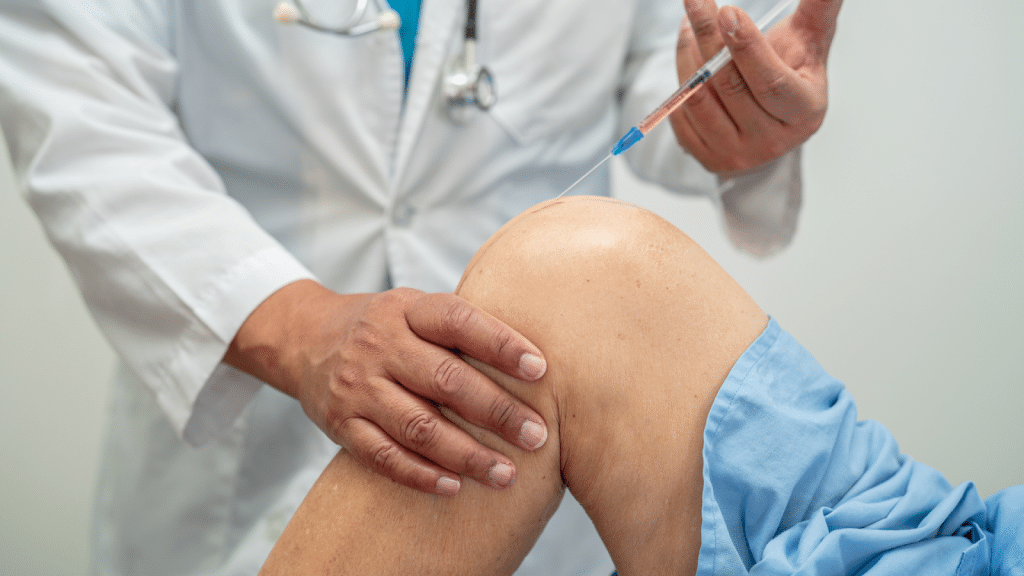 A doctor wearing a white lab coat is administering an injection into a patient's knee. The patient's leg is partially covered with a blue drape, and the doctor's stethoscope is visible around their neck.