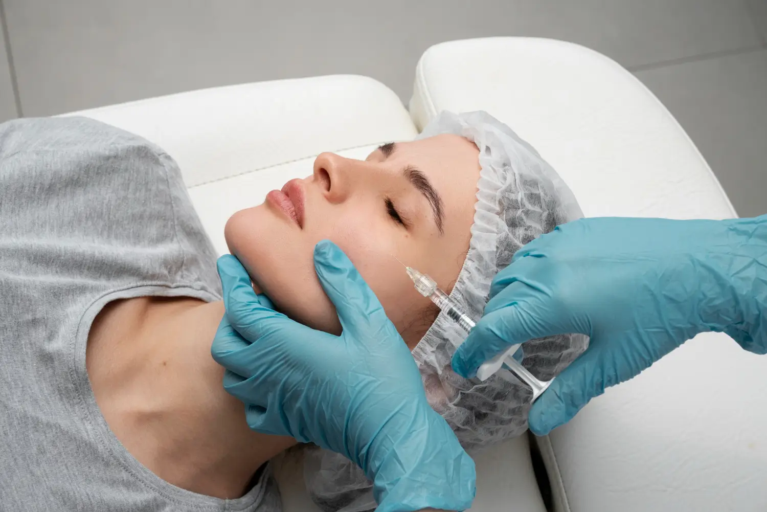 A patient laying on a bed as a healthcare professional administers facial filler treatment.